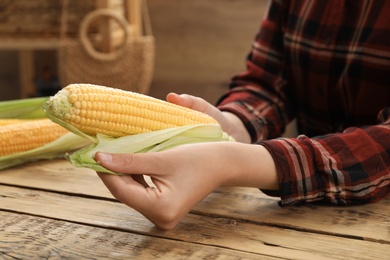 Photo of Woman husking corn cob at wooden table, closeup