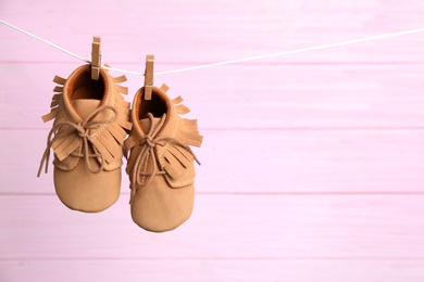 Pair of shoes on laundry line against pink wooden background, space for text. Baby accessories