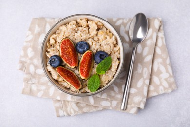 Oatmeal served with blueberries, mint and fig pieces on light grey table, top view