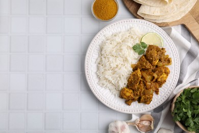 Photo of Delicious chicken curry with rice and ingredients on white tiled table, flat lay. Space for text