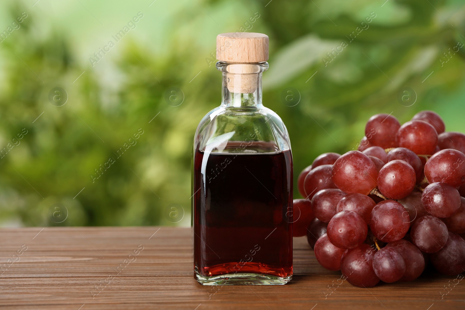 Photo of Bottle with wine vinegar and fresh grapes on wooden table against blurred background. Space for text