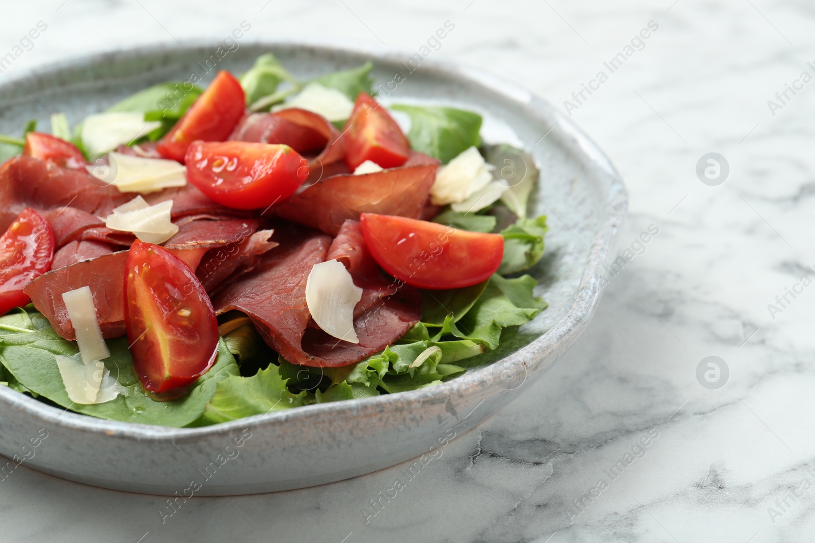 Photo of Delicious bresaola salad with tomatoes and parmesan cheese on white marble table, closeup