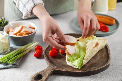 Woman cooking delicious pita wrap with chicken and lettuce at light gray table, closeup