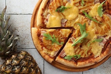 Photo of Delicious cut pineapple pizza and ripe fruit on light gray tiled table, flat lay