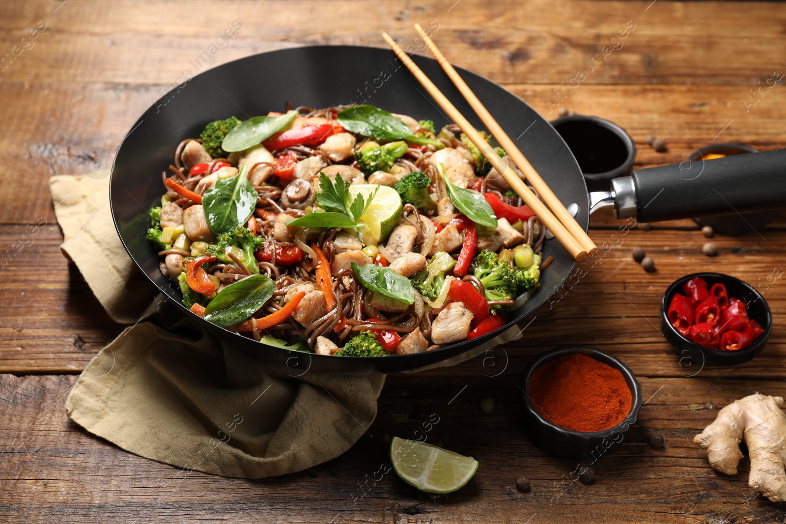 Photo of Stir-fry. Tasty noodles with meat in wok, chopsticks and ingredients on wooden table