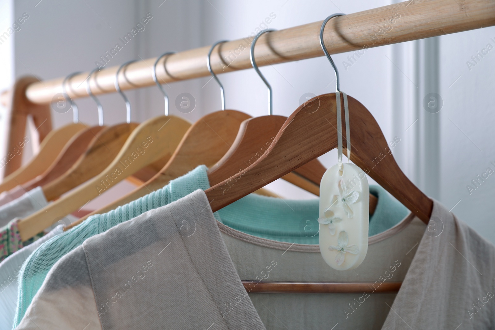 Photo of Beautiful scented wax sachet and clothes hanging on wooden rack indoors