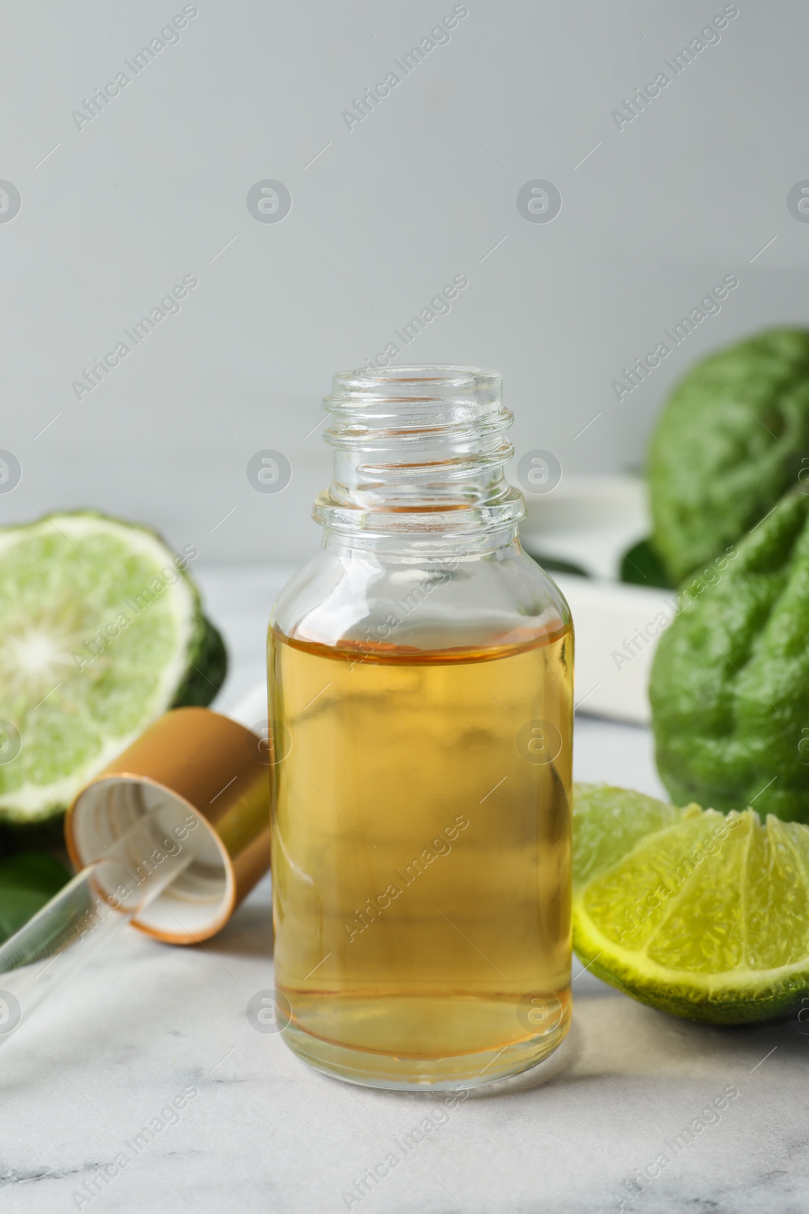 Photo of Bottle of essential oil, pipette and fresh bergamot fruits on white marble table