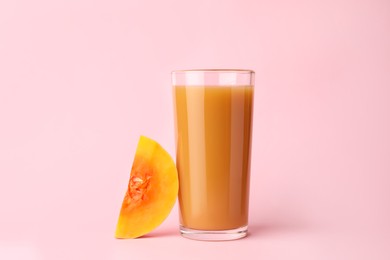 Photo of Tasty pumpkin juice in glass and cut pumpkin on pink background
