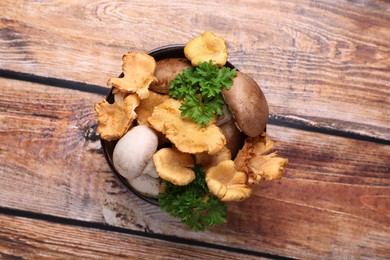 Bowl of different mushrooms and parsley on wooden table, top view