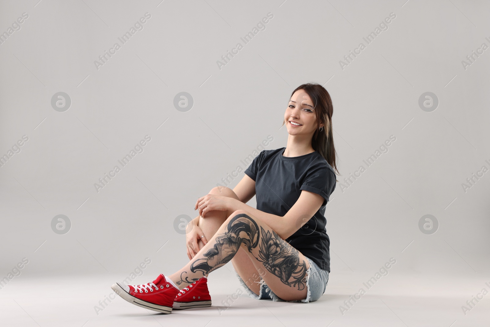 Photo of Smiling tattooed woman posing on grey background