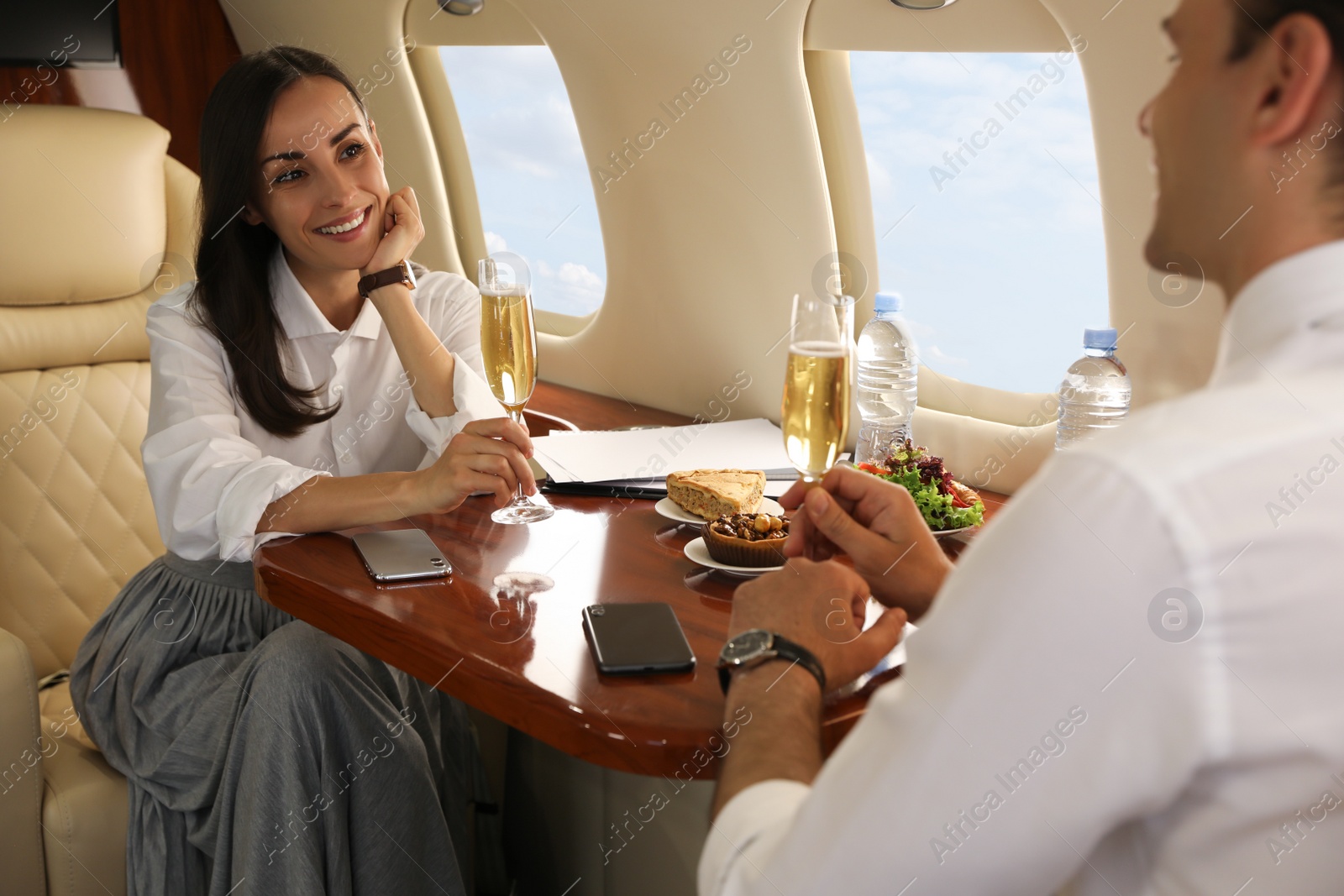 Photo of Colleagues with glasses of champagne at table in airplane during flight