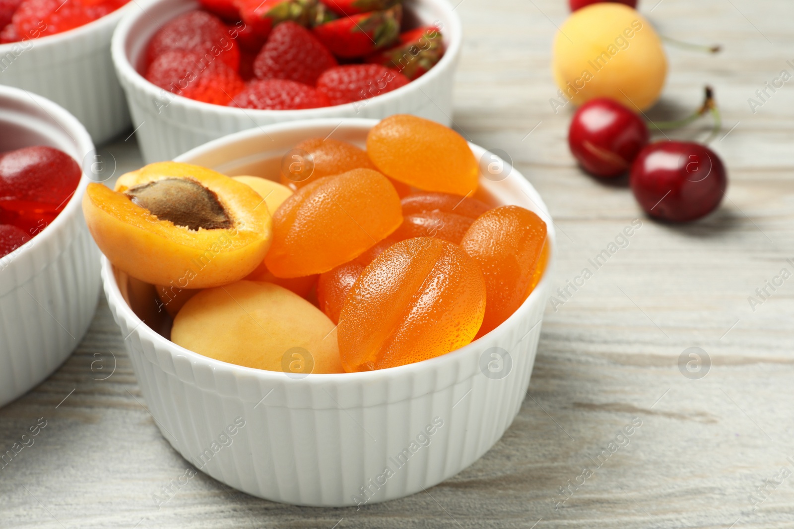 Photo of Delicious gummy candies and fresh fruits on white wooden table, closeup