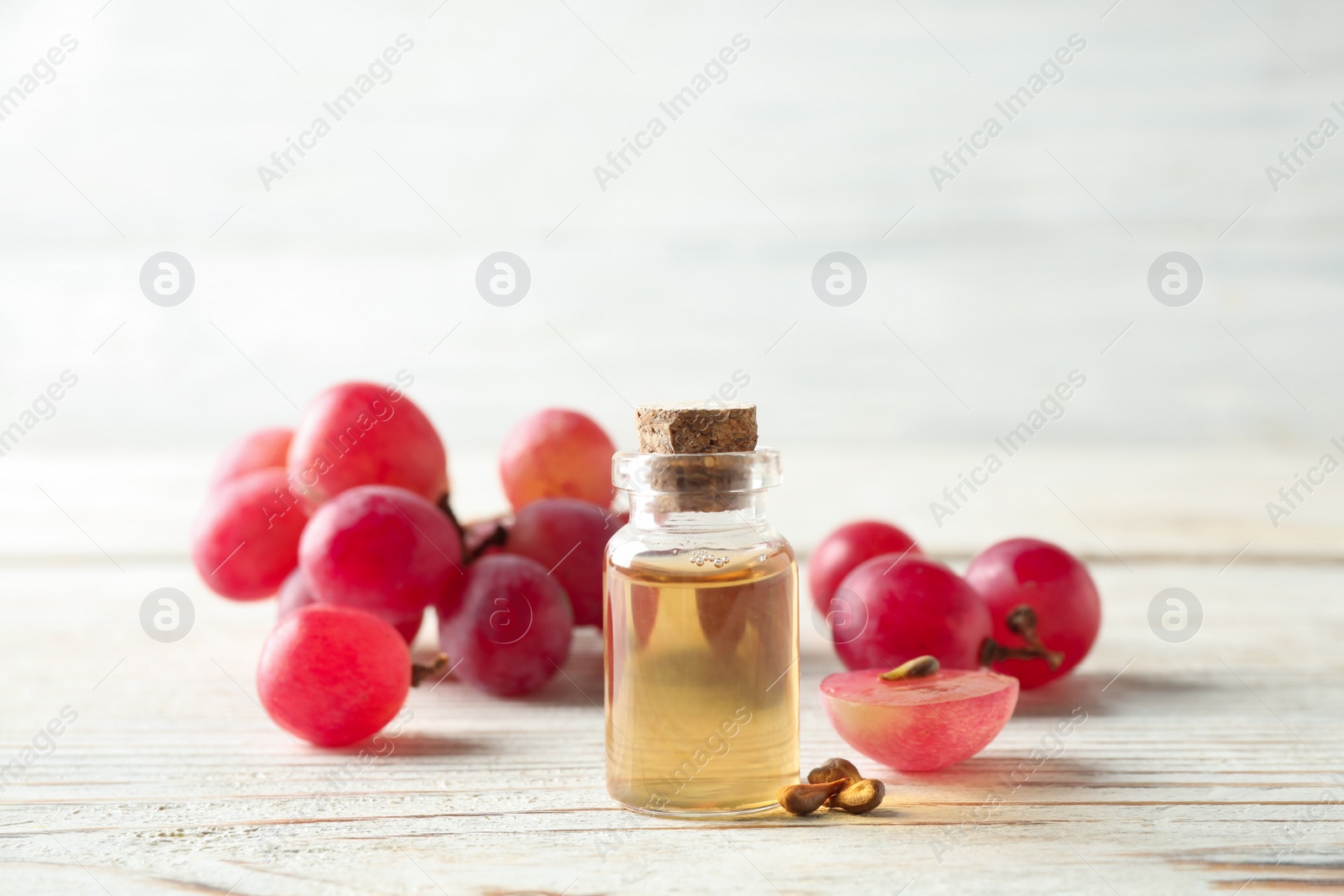 Photo of Organic red grapes, seeds and bottle of natural essential oil on white wooden table