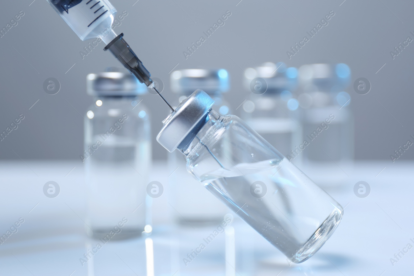 Photo of Filling syringe with medicine from vial on white table, closeup