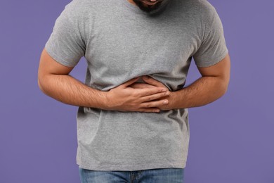 Young man suffering from stomach pain on purple background, closeup