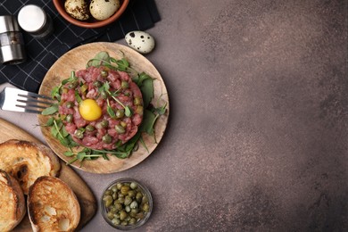 Photo of Tasty beef steak tartare served with yolk, capers and bread on brown table, flat lay. Space for text