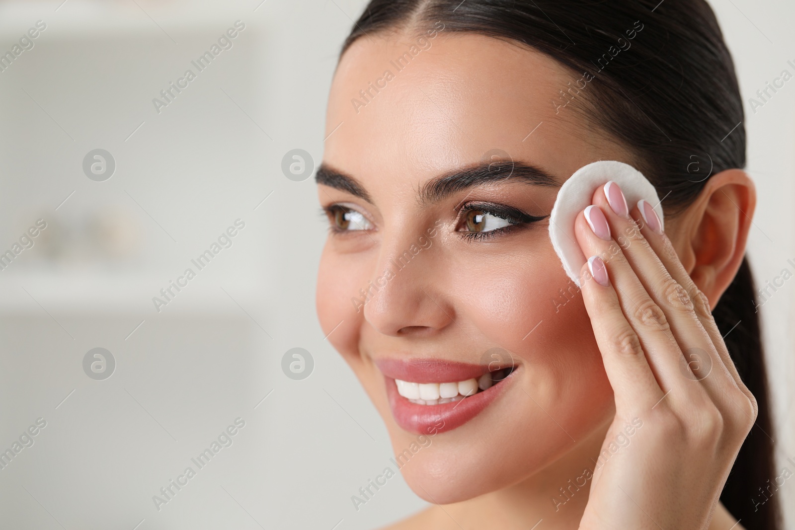 Photo of Beautiful woman removing makeup with cotton pad indoors, closeup. Space for text