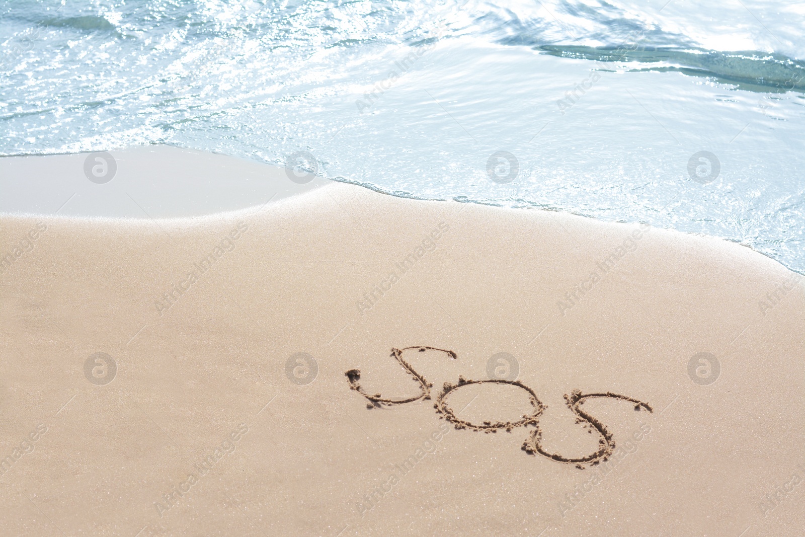 Photo of Message SOS drawn on sandy beach near sea