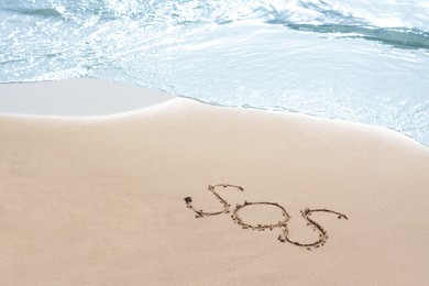 Photo of Message SOS drawn on sandy beach near sea