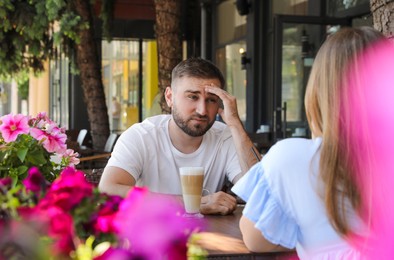Photo of Young man having boring date with girl in outdoor cafe