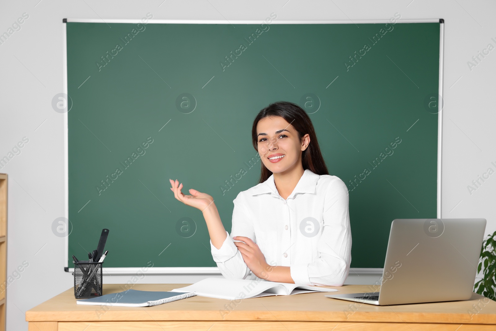 Photo of Young teacher giving lesson at table in classroom