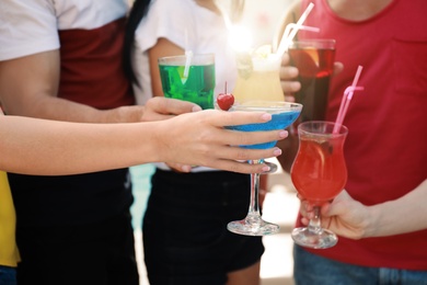 Photo of Friends clinking glasses with fresh summer cocktails outdoors, closeup