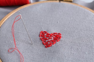 Embroidered red heart and needle on gray cloth, closeup