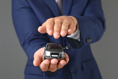 Insurance agent holding toy car on gray background, closeup