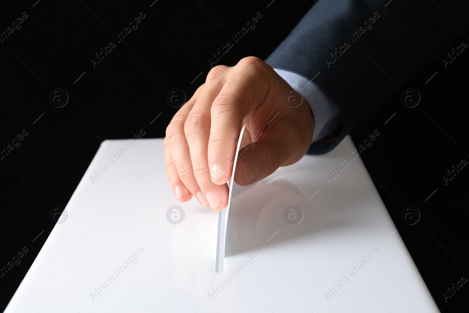 Photo of Man putting his vote into ballot box on black background, closeup