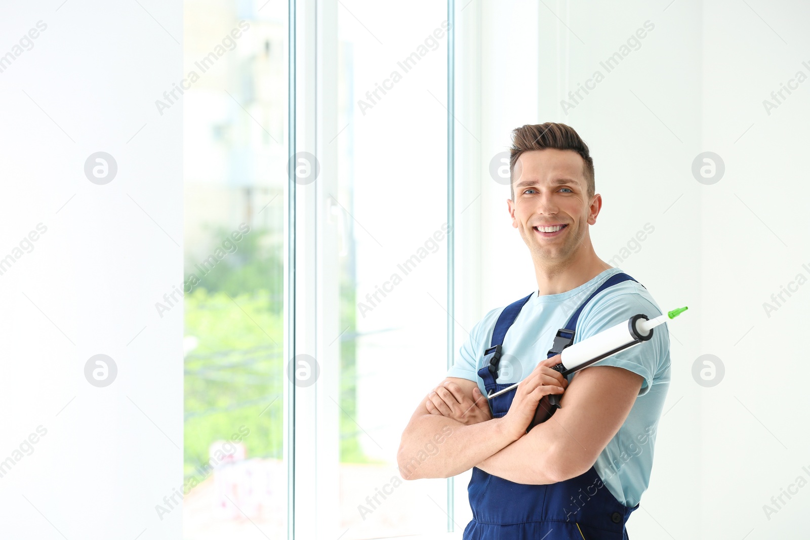 Photo of Construction worker in uniform with window sealant indoors