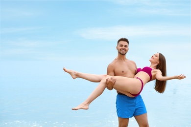 Photo of Young man holding his girlfriend in bikini on beach, space for text. Lovely couple