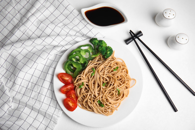 Photo of Tasty buckwheat noodles with fresh vegetables served on white table, flat lay