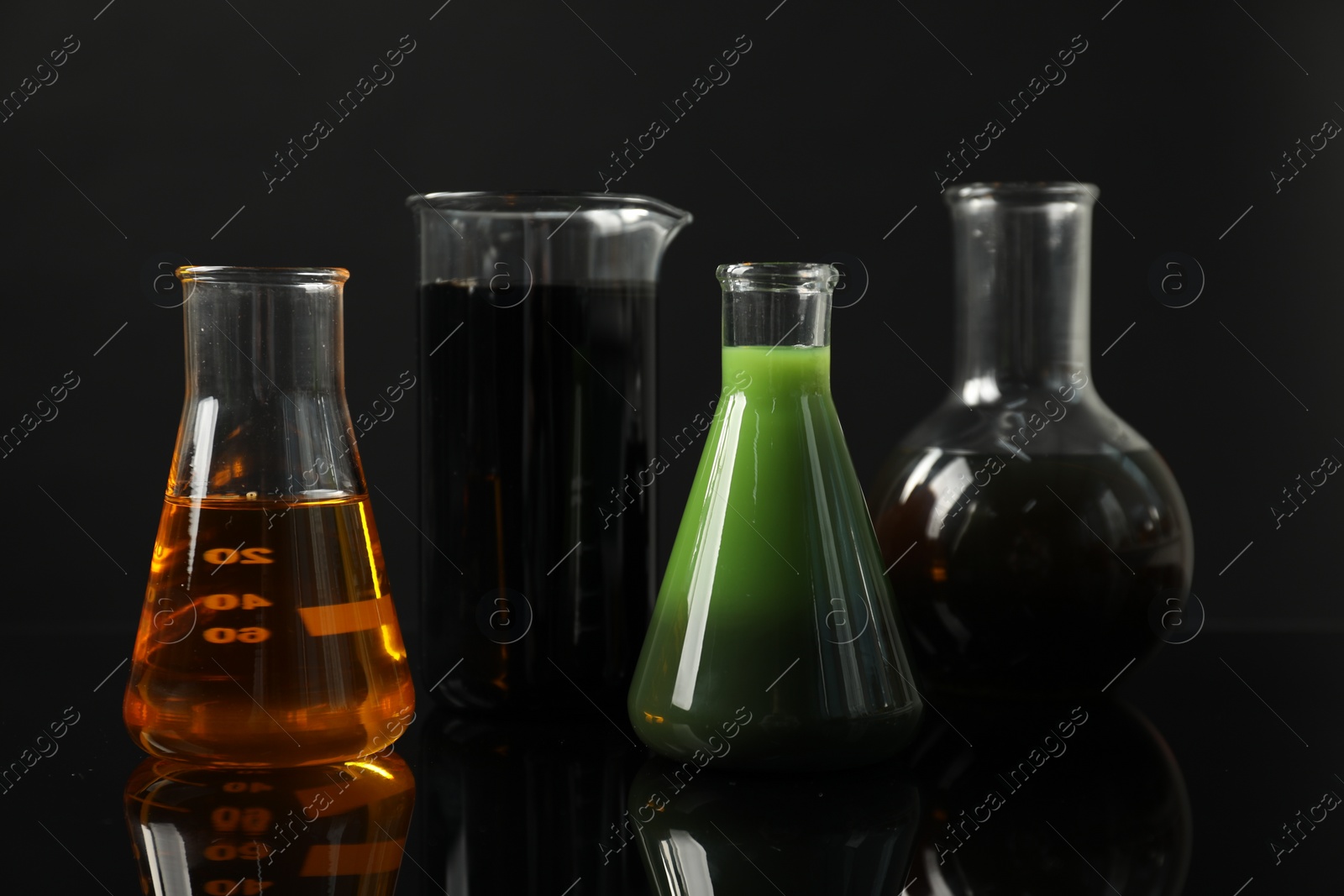 Photo of Glass flasks and beaker with different types of oil on black background