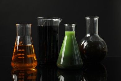 Photo of Glass flasks and beaker with different types of oil on black background