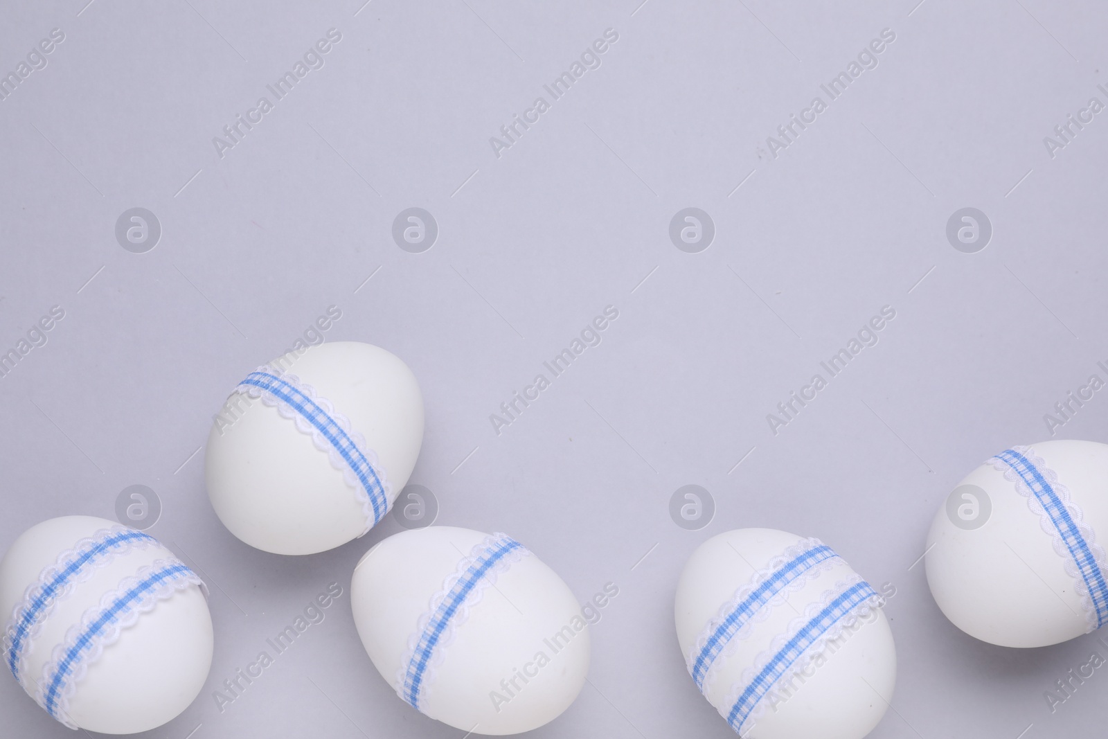 Photo of Beautifully decorated Easter eggs on light grey background, flat lay. Space for text