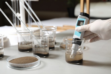 Scientist measuring acidity and pH of soil at table, closeup. Laboratory analysis