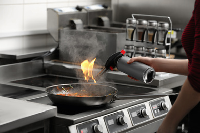 Photo of Female chef with manual gas burner cooking tasty food on stove in restaurant kitchen, closeup