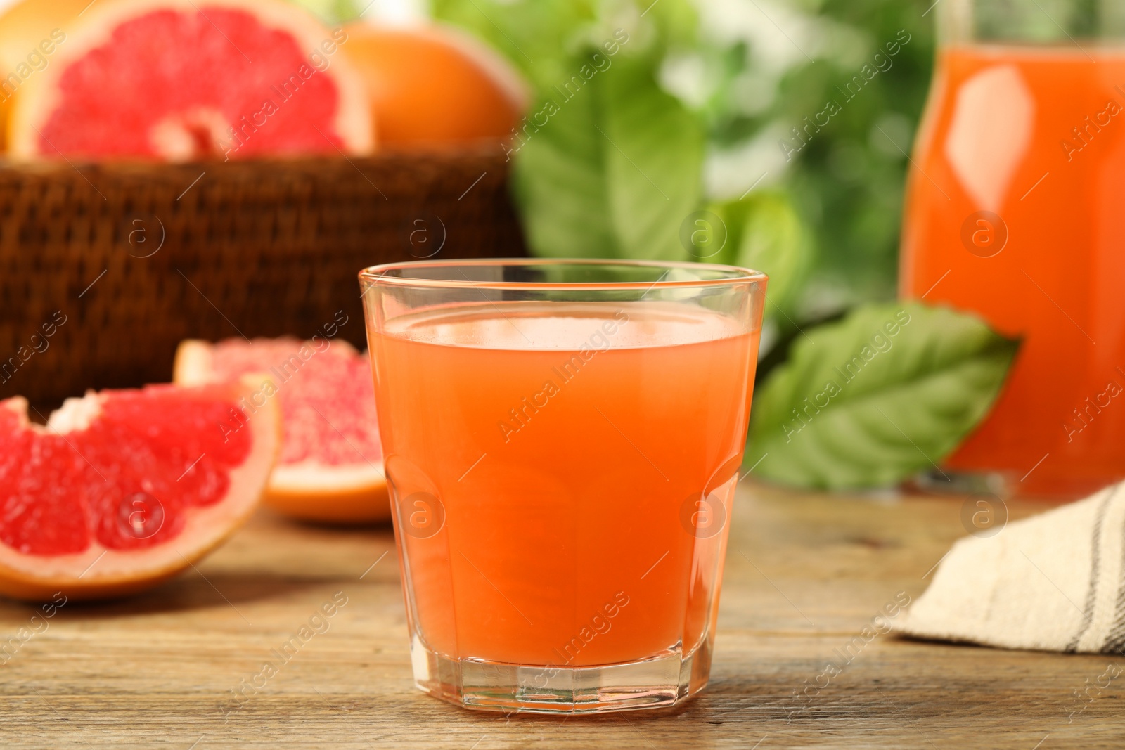 Photo of Glass of delicious grapefruit juice on wooden table against blurred background