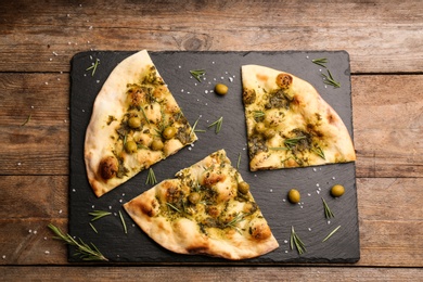 Traditional Italian focaccia bread with guacamole, olives and rosemary on wooden table, top view