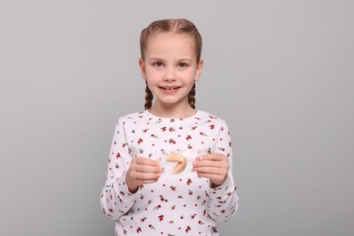 Photo of Cute girl holding tasty fortune cookie with prediction on light grey background