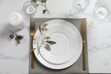 Photo of Stylish setting with cutlery, burning candle and eucalyptus leaves on white marble table, flat lay