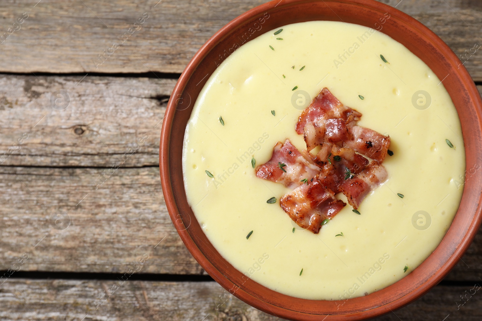 Photo of Tasty potato soup with bacon and rosemary in bowl on wooden table, top view. Space for text