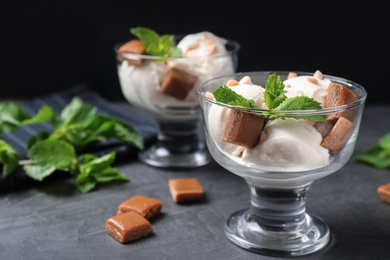Photo of Glass bowls of ice cream with caramel candies and mint on grey table