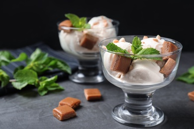 Glass bowls of ice cream with caramel candies and mint on grey table