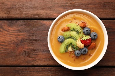 Photo of Delicious smoothie bowl with fresh berries, kiwi and nuts on wooden table, top view. Space for text