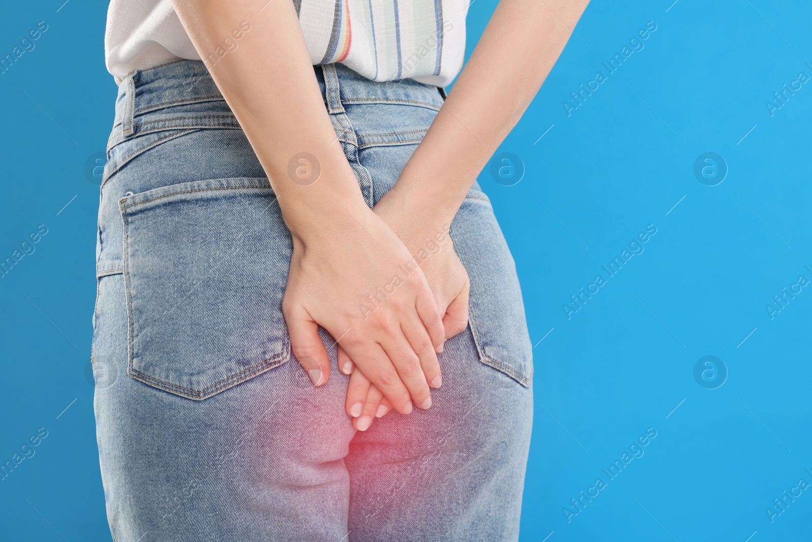 Image of Woman suffering from hemorrhoid on light blue background, closeup