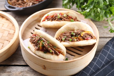 Photo of Delicious gua bao in bamboo steamer on wooden table