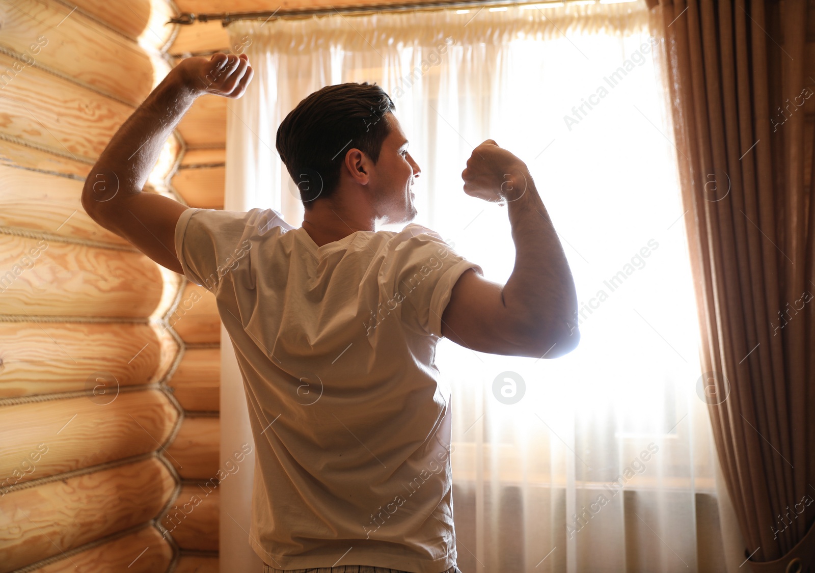 Photo of Man stretching near window indoors. Lazy morning