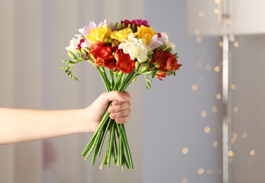 Photo of Woman holding bouquet of beautiful spring freesia flowers in room