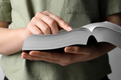 Woman reading holy Bible against light grey background, closeup